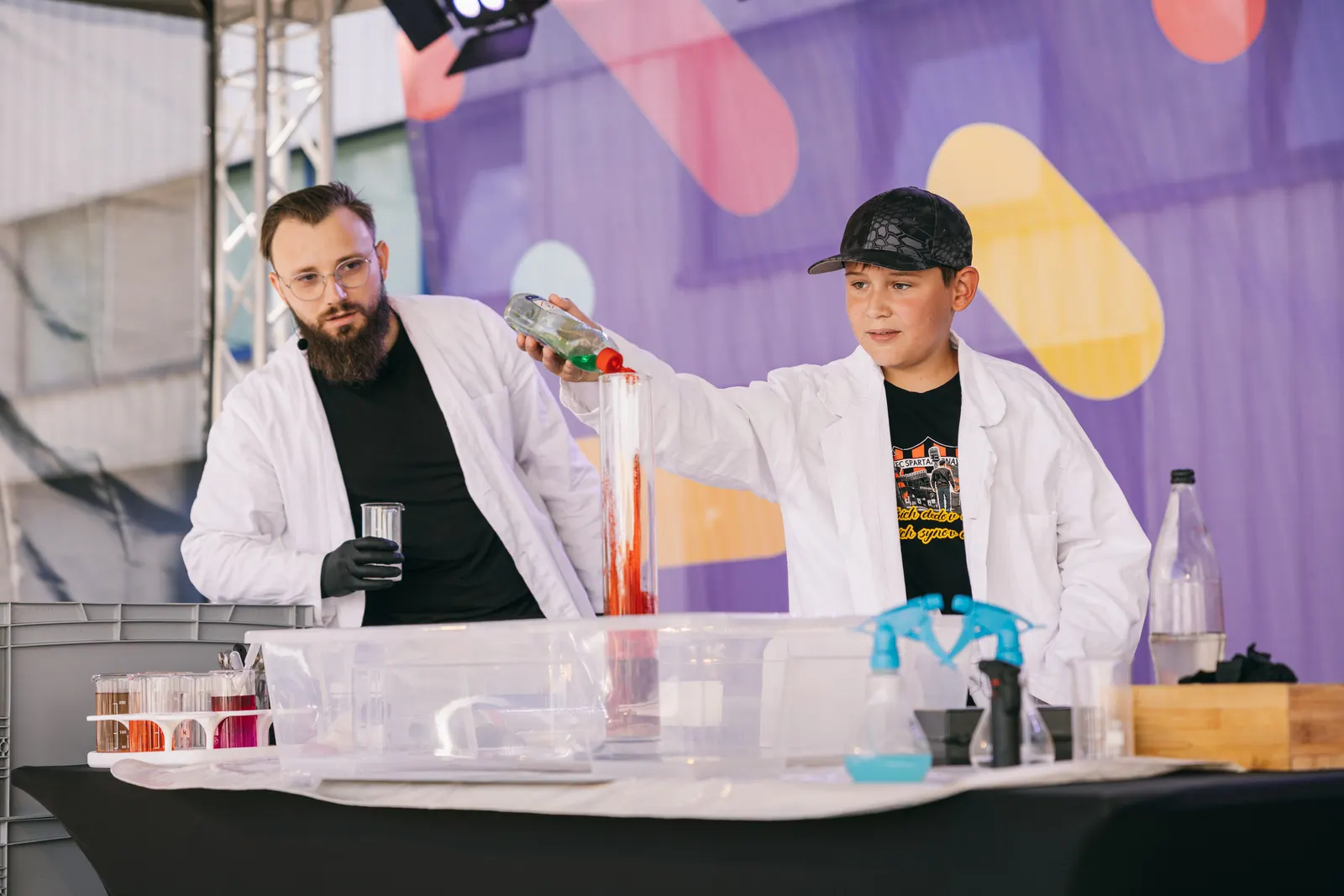 Chemik a mladý asistent robia pokus na pódiu firemného dňa