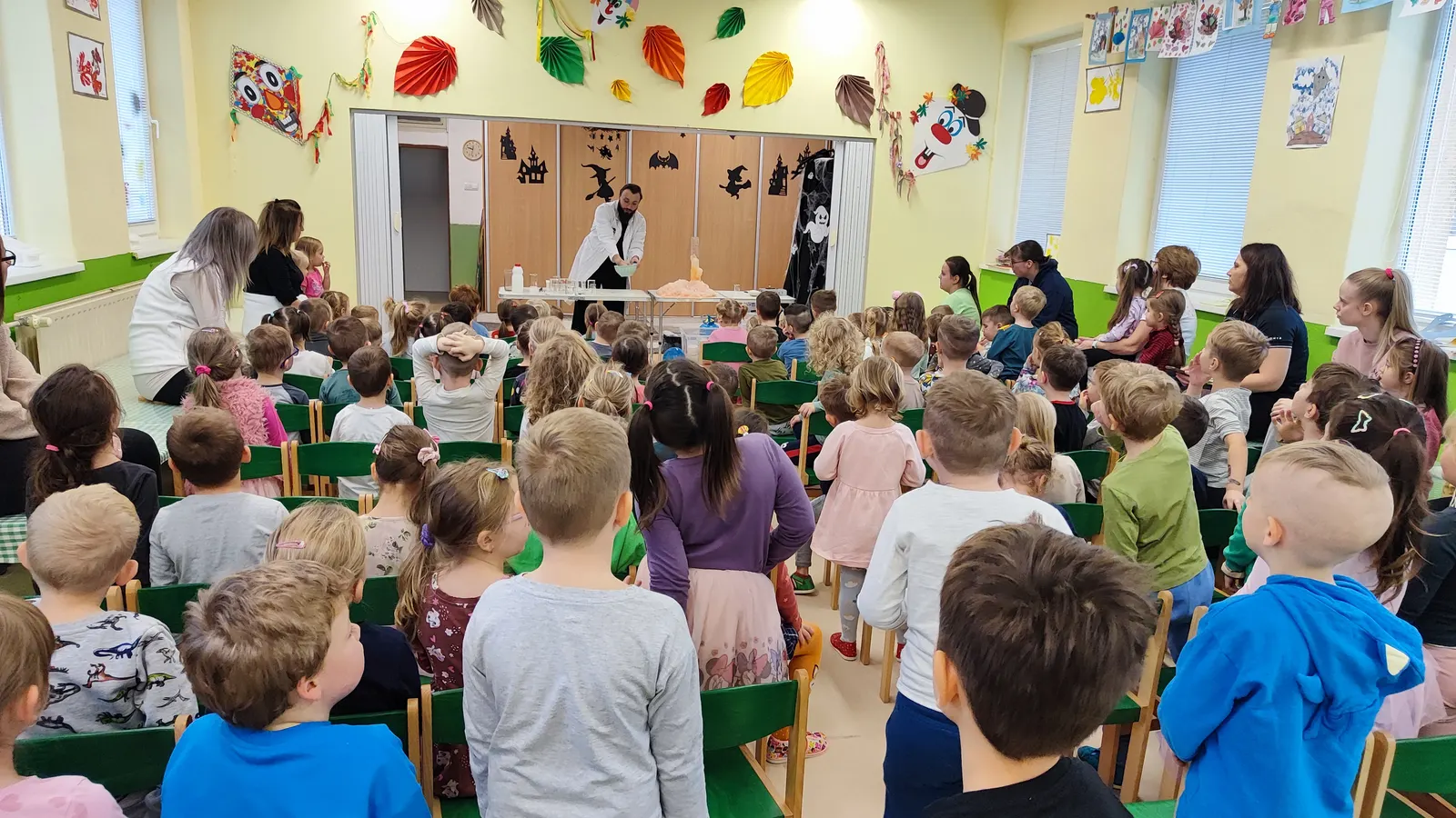 Deti v škôlke sedia a sledujú vedeckú show