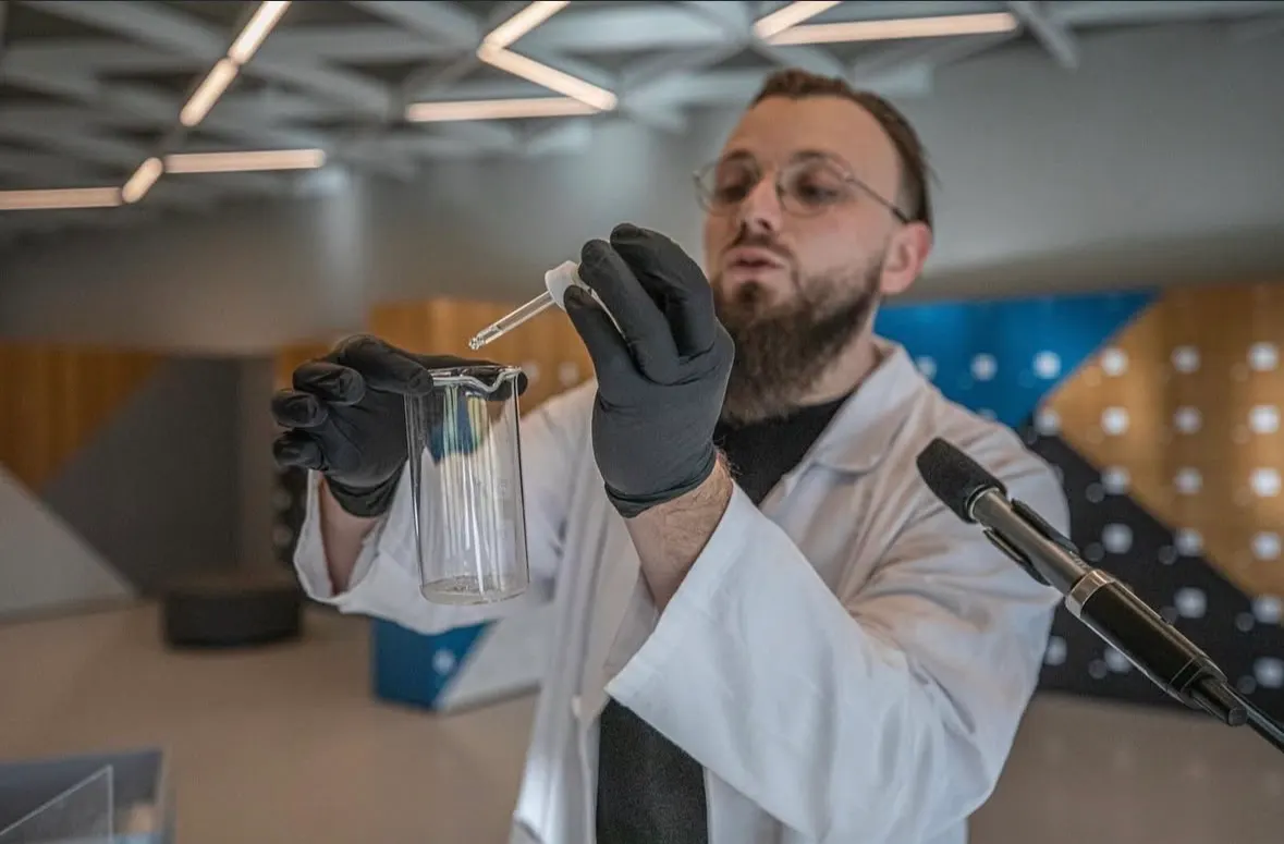 Chemik pri mikrofóne kvapká pipetou do kadičky