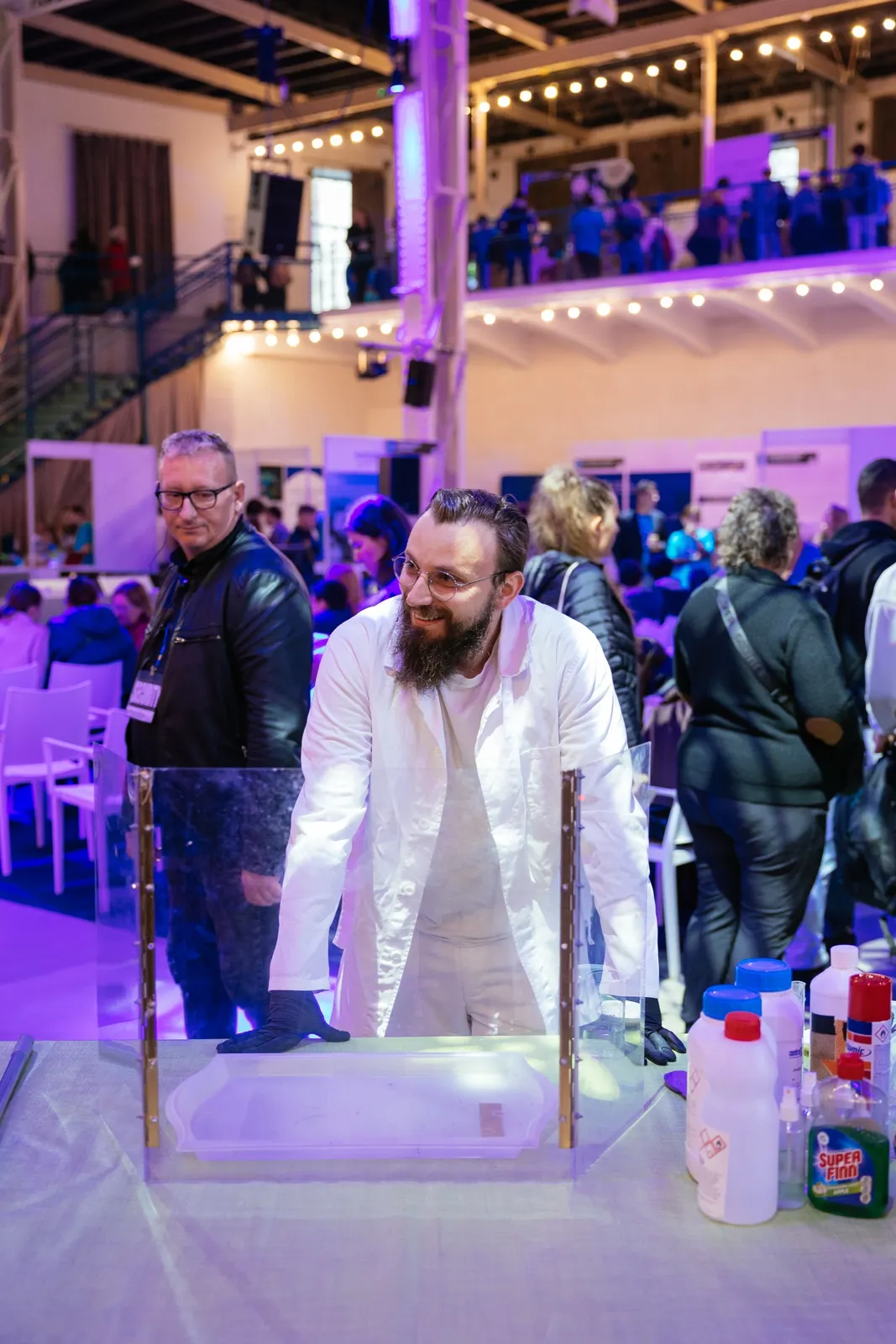 Chemik robí pokus uprostred návštevníkov v sále s fialovým svetlom